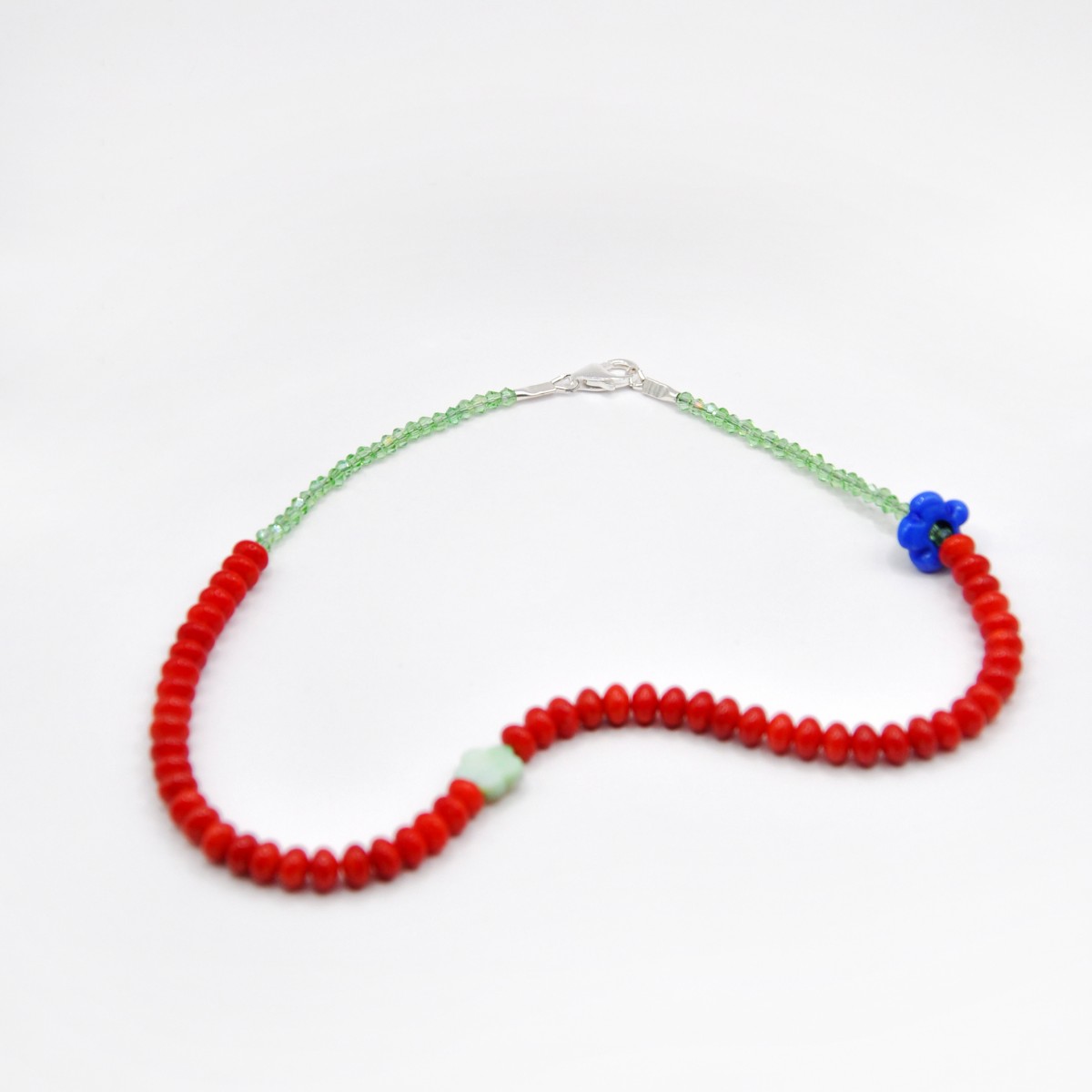 »Blumengarten« – Kette aus roten Edelsteinen und zweierlei Blüten: eine schimmernde Perlmuttblume in der Mitte und eine blaue Glasblüte an der Seite von pinapina