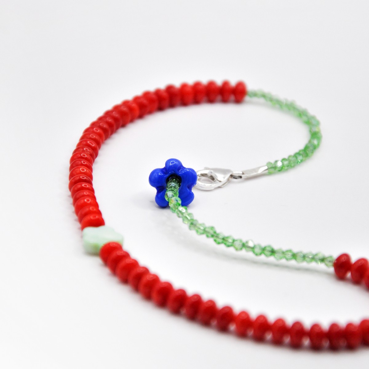 »Blumengarten« – Kette aus roten Edelsteinen und zweierlei Blüten: eine schimmernde Perlmuttblume in der Mitte und eine blaue Glasblüte an der Seite von pinapina